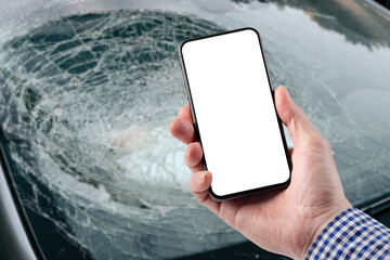 A man holds a smartphone in his hand. Broken car glass and deployed driver's airbag.