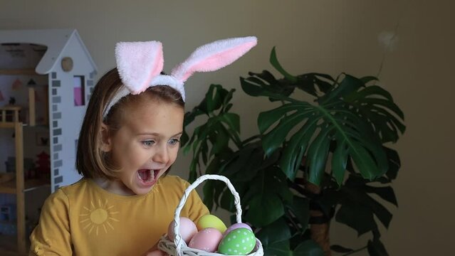 Easter egg hunt. Excited emotion surprise adorable child girl in bunny ears rabbit costume hold basket with Easter colored eggs. Children positive emotions. Kid happy Easter