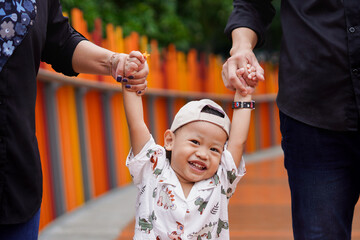 Cheerful boy facing Camera, Smiling, Held by Hands of Parents at the Park
