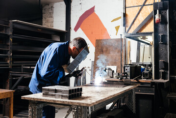 Anonymous man using steel mask while welding metal in factory