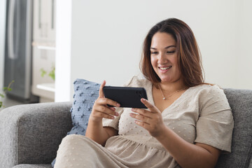 Young plus size biracial woman enjoys gaming on her phone at home, with copy space unaltered