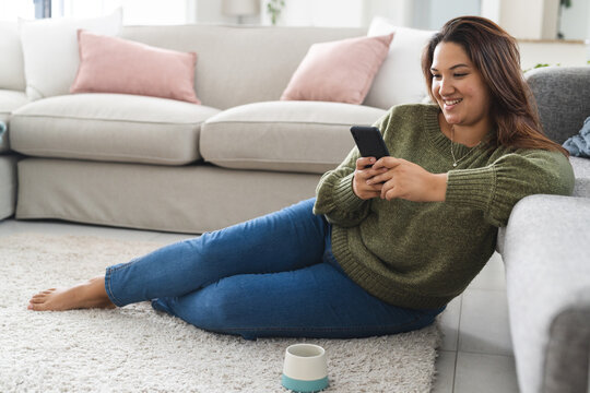 Young plus size biracial woman enjoys leisure time at home, comfortably using her smartphone while s - Powered by Adobe