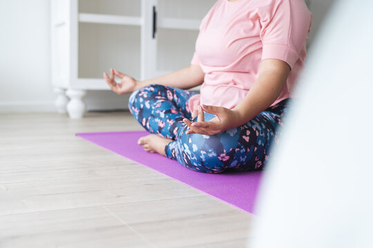 Young plus size biracial woman practices yoga at home, on a purple mat unaltered