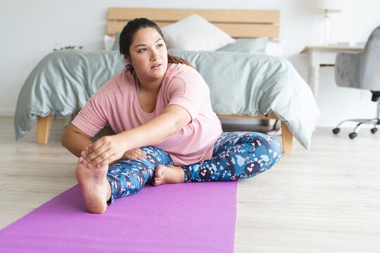 Young plus size biracial woman stretches on a yoga mat at home - Powered by Adobe
