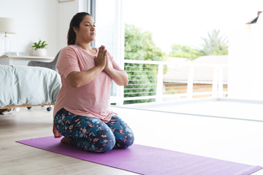 Young plus size biracial woman practices yoga at home, on a purple mat unaltered - Powered by Adobe