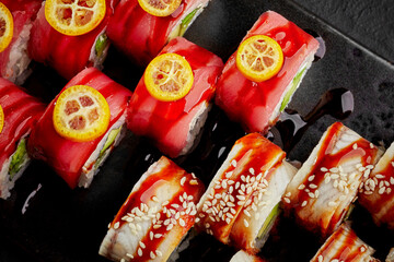 Vibrant sushi rolls with tuna, eel, kumquat and sesame on dark slate