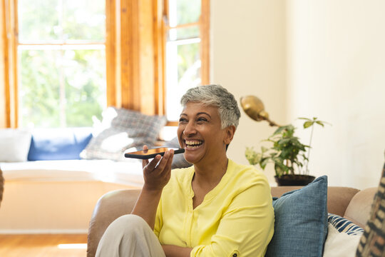 Mature biracial cheerful woman using voice command on smartphone at home