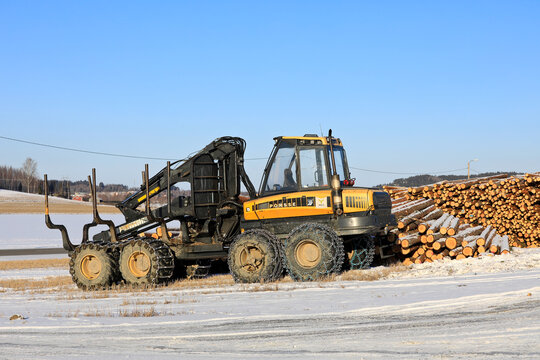 Ponsse Wisent forestry forwarder with snow chains on tires and stacked pine logs at work site in winter. Copy space. 