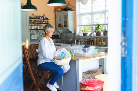 A mature biracial woman sorts recycling at home, with copy space