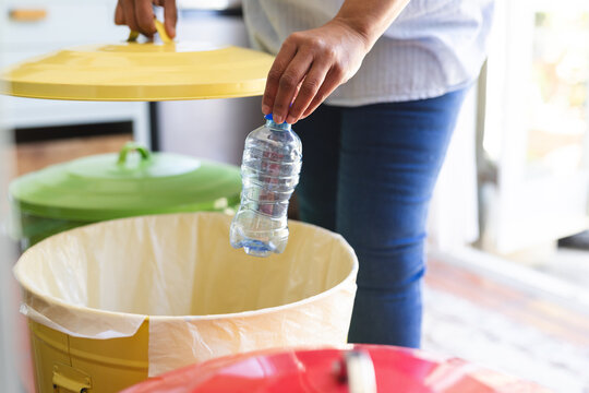 A mature biracial woman engages in recycling at home, with copy space
