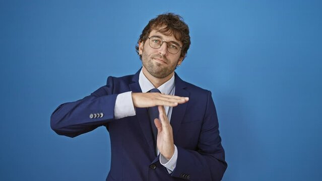 Frustrated young businessman in suit gives 'time out', hands-up gesture. isolated on a blue background, he's had enough and demands a break!