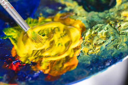 A close-up of a paintbrush mixing colors on a palette