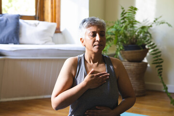 A mature biracial woman practices yoga at home