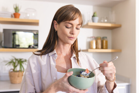 A young Caucasian woman enjoys a healthy meal from a bowl