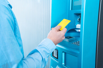 A man is inserting a blue credit card into a plastic ATM machine in a room filled with electric...