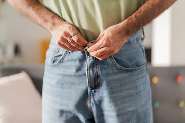Midsection of a man wearing blue jeans with a green shirt slightly raised, revealing the waistband