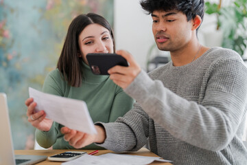 A young man captures an image of a paper document using his smartphone, with a focused expression as a woman looks on. The scene suggests a moment of sharing information or digitizing paperwork