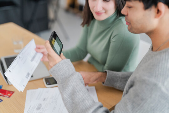 Close-up of a couple using a smartphone to scan a bill to pay with home banking at a home office