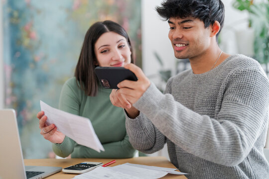A young man captures an image of a paper document using his smartphone, with a focused expression as a woman looks on. The scene suggests a moment of sharing information or digitizing paperwork