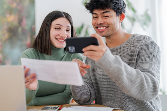 A young man captures an image of a paper document using his smartphone, with a focused expression as a woman looks on. The scene suggests a moment of sharing information or digitizing paperwork