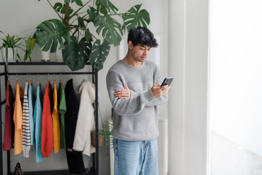 A young man stands by a window, lost in thought while talking on the phone. His casual attire and contemplative demeanor suggest a personal conversation