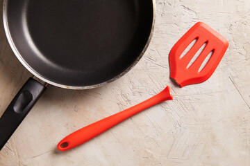 Broken red spatula with a frying pan on a textured background