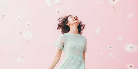 Obraz na płótnie Canvas Woman in a pastel mint dress laughing, surrounded by floating dandelions on a light pink background