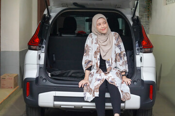 Young Asian muslim woman sitting on the back of her car getting ready to go to vacation.