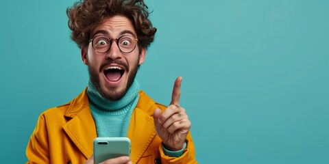 Happy young man holding a smartphone with a cheerful expression on his face, representing modern communication and success on a blue background.