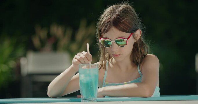 Teenage girl crushes ice in a cocktail on the side of the pool