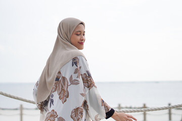 Pretty muslim woman enjoying sun shine at the beach wearing cardigan.