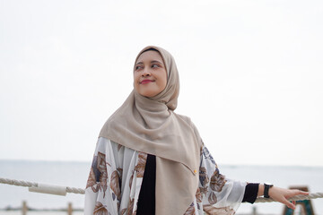 Pretty muslim woman enjoying sun shine at the beach wearing cardigan.