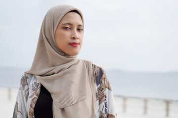 Pretty muslim woman enjoying sun shine at the beach wearing cardigan.