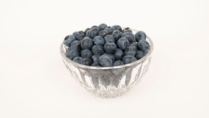 Ripe blueberries in a glass bowl on white background.
