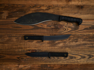 Close-up of three different fixed-blade knives with black blades and black handles. All laid out on...