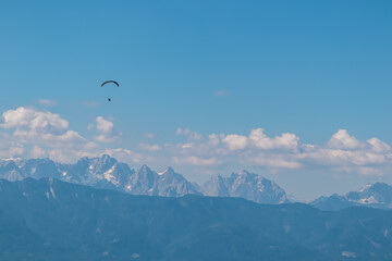 Person paragliding over alpine landscape with panoramic view of majestic mountain range Julian Alps seen from Gerlitzen Alpe, Carnthia, Austria. Dangerous adrenaline sport. Leisure activity in summer