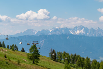 Ski lift in summer with scenic view of majestic mountain range Julian Alps seen from Gerlitzen, Carinthia, Austria. Wanderlust in Austrian Alps. Idyllic hiking trail along alpine meadow and forest