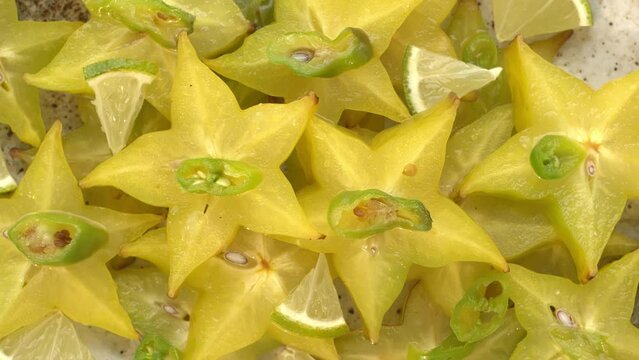 Top view of carambola or star fruit spicy salad with frozen green chili, lime pieces, and and lime juice. Perfect condiment for grilled fish or a curry. Table spin.