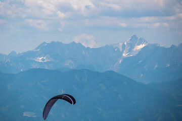 Person paragliding over alpine landscape with panoramic view of majestic mountain range Julian Alps...