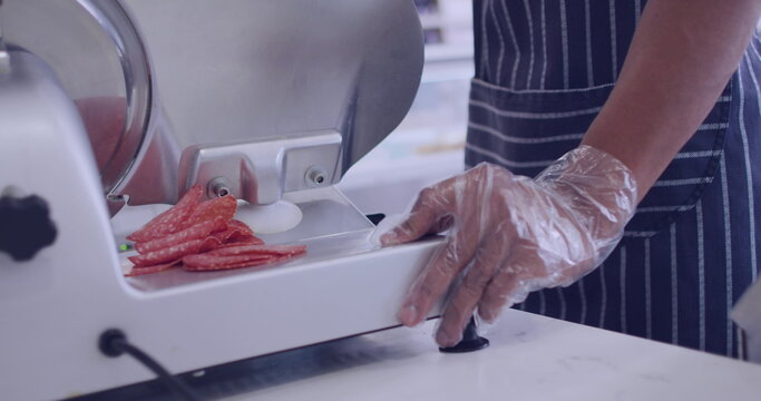 Person slices salami on a meat slicer at a deli - Powered by Adobe