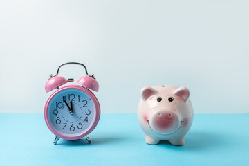 Piggy bank with alarm clock on blue table. Christmas or New Year minimal concept.