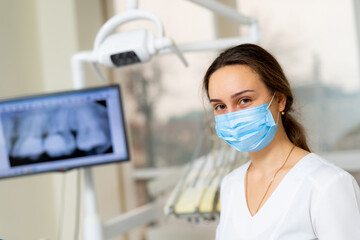 Fototapeta na wymiar Young female dentist is wearing mask and standing in front of dental x-ray in dental office.