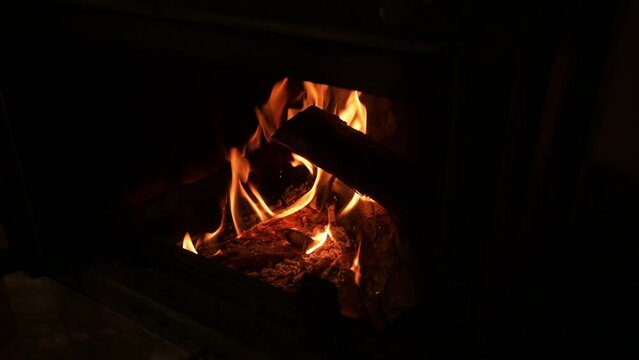 The man puts a log into the fireplace with his hand where the firewood is burning. Closing the glass door of the fireplace. 