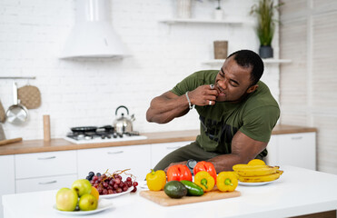 African American man sitting at the table in kitchen and eating healthy food