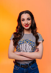 Portrait of smiling young woman with crossed arms standing isolated over orange background