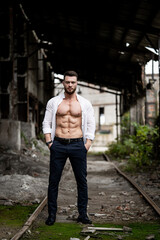 Fototapeta na wymiar Handsome muscular man stands on the tracks in abandoned factory