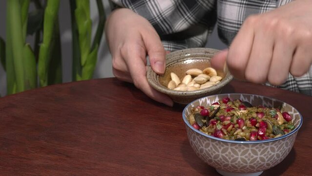 Woman sprinkles freekeh salad  with roasted almonds. Potted plant on the side.