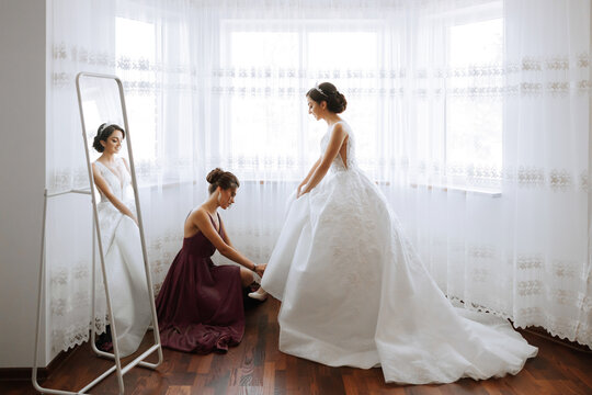 The bridesmaid is happy in the morning, helping to fasten the buttons on the wedding dress and prepare for the wedding ceremony. They take pictures, smile, help the bride with her shoes.