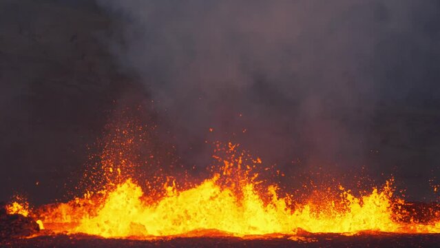 Close-up camera shot of volcanic eruption. Lava coming from the ground. Orange, yellow color magma. Smokes above boiling lava.