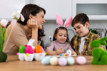 Happy Family Painting Easter Eggs On Kitchen Table. Mother son and daughter painting eggs. Happy family preparing for Easter. Cute little child girl wearing bunny ears.